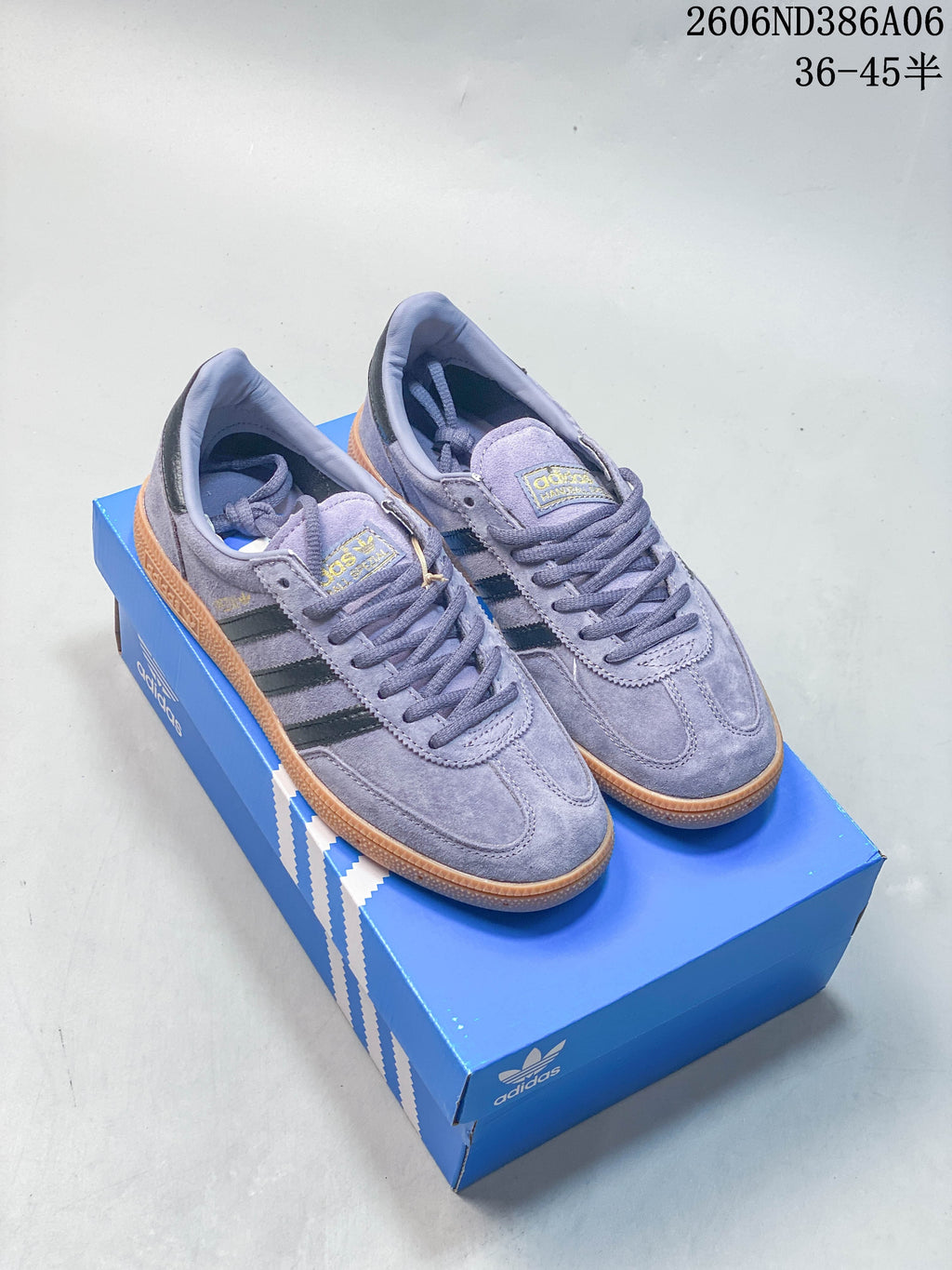 Lavender and burgundy Adidas Handball Spezial low-top sneakers shown together on a blue shoe box