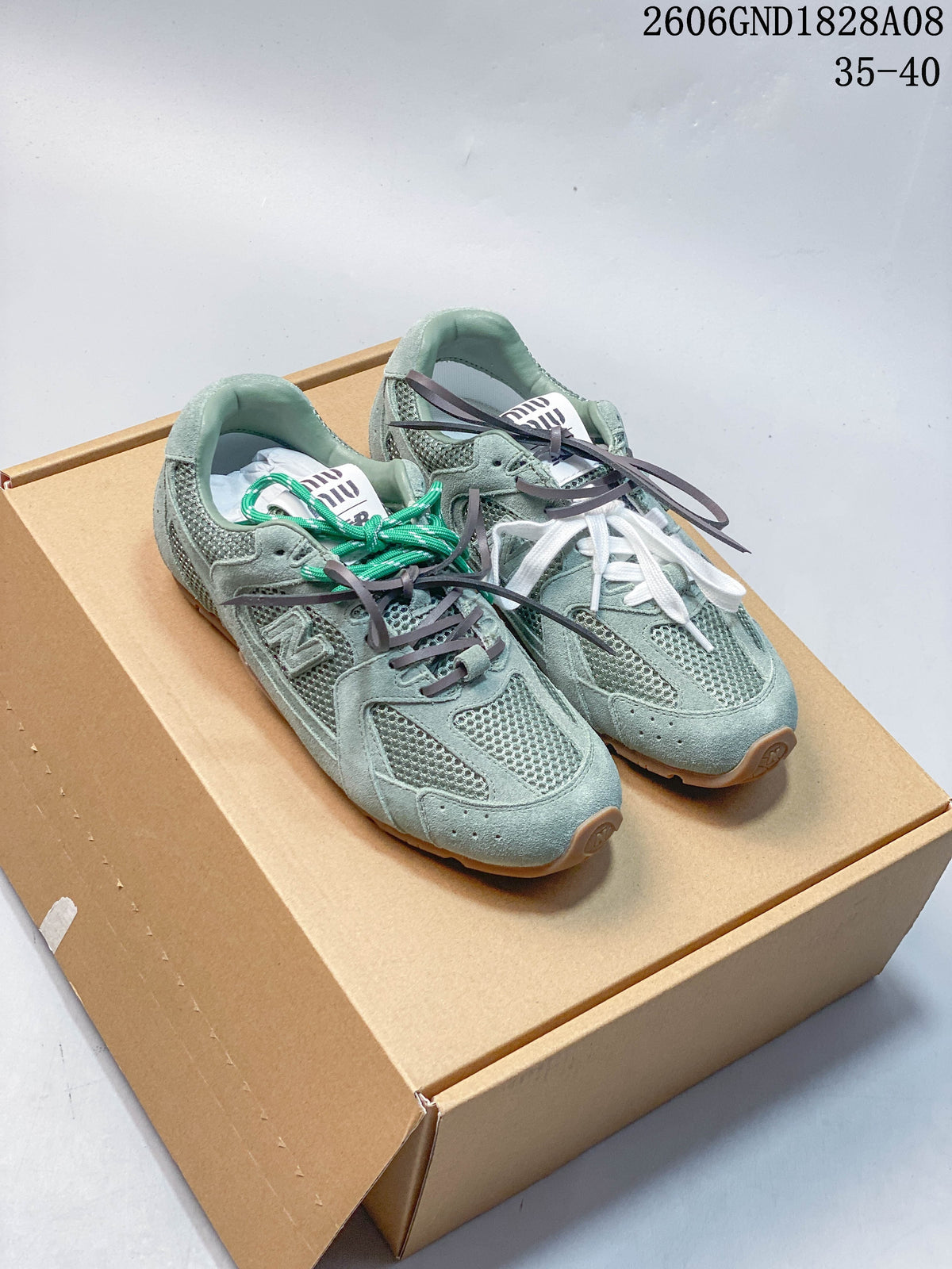Pair of muted green sneakers with mesh panels and mixed-color laces on a box.