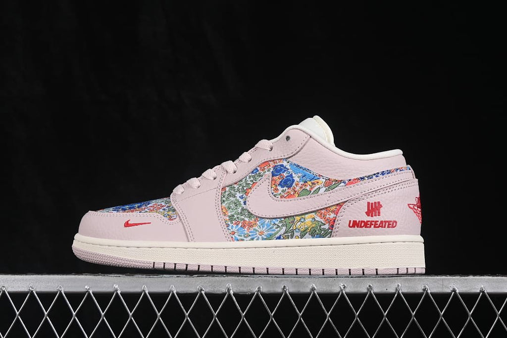 Side view of a pale pink low-top sneaker with floral-patterned panels and red logo details