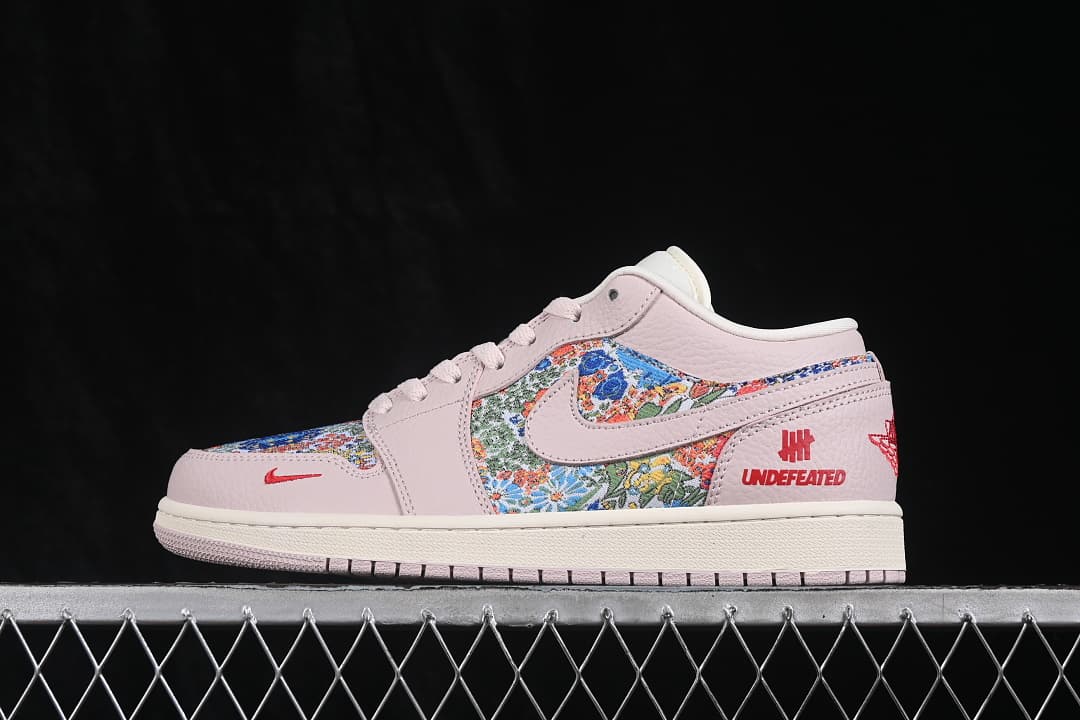 Side view of a pale pink low-top sneaker with floral-patterned panels and red logo details