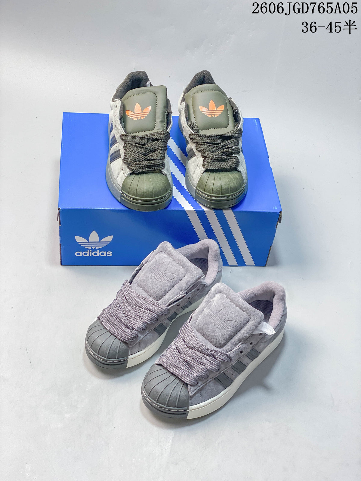 Green and grey Adidas Originals Superstar XLG sneakers shown together on and beside a blue shoe box.