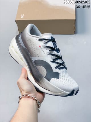 ON Cloudboom Max shoe shown from a side angle in white, gray, and black, with the shoe box behind it.