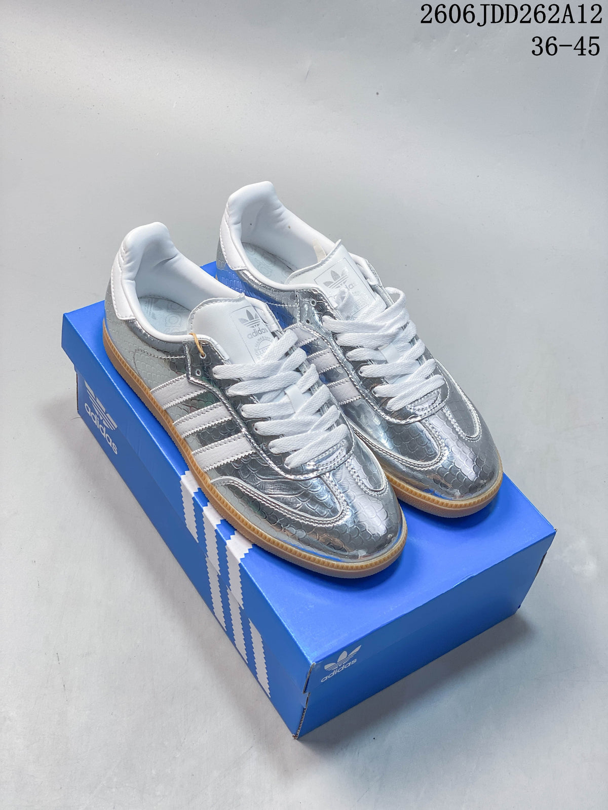 Pair of silver low-top sneakers with white stripes and gum-colored soles on a blue box.