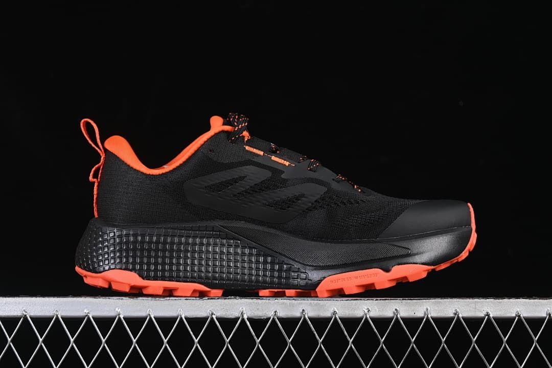 Side view of a black shoe with orange collar trim and outsole.