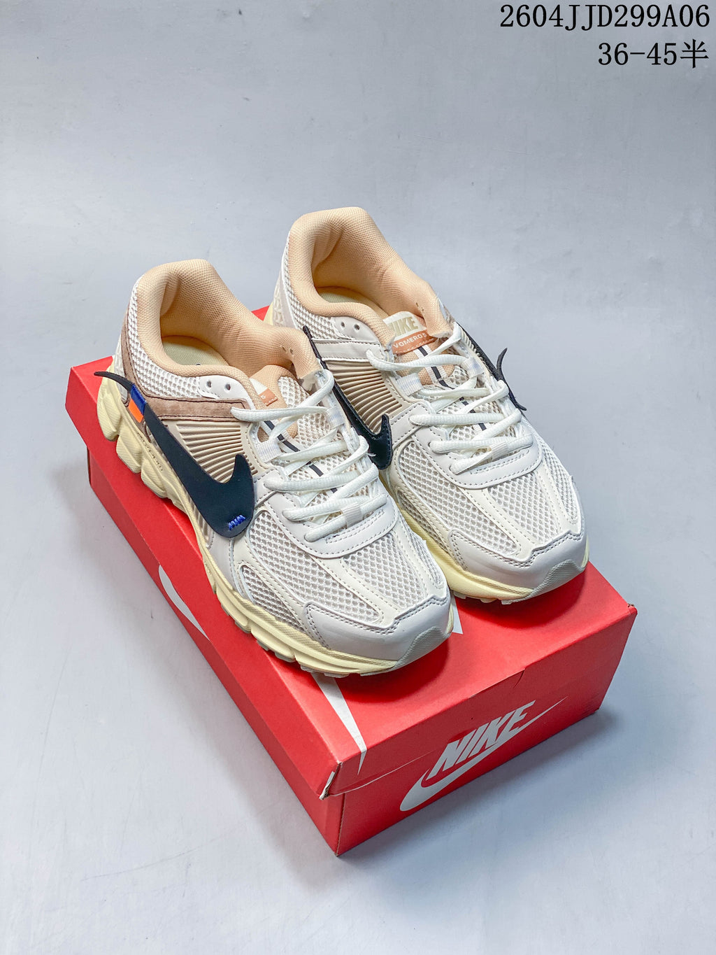 Pair of light-colored Nike Zoom Vomero 5 sneakers with dark Swoosh accents, photographed from the front on a red shoe box.