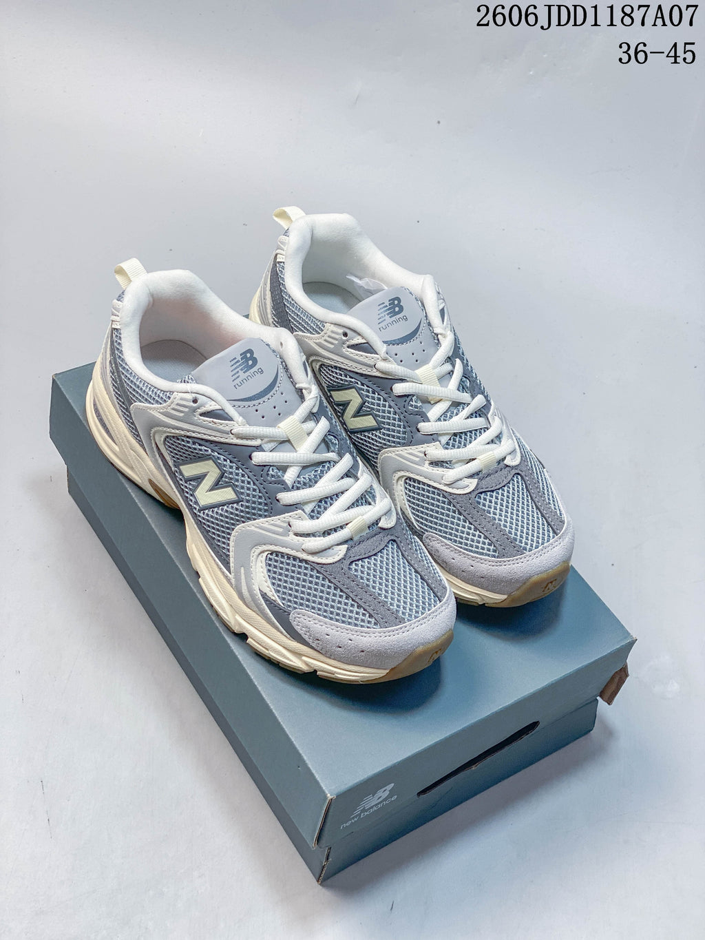 Pair of grey and blue-grey New Balance 530-style mesh sneakers with off-white accents, shown on a shoe box.