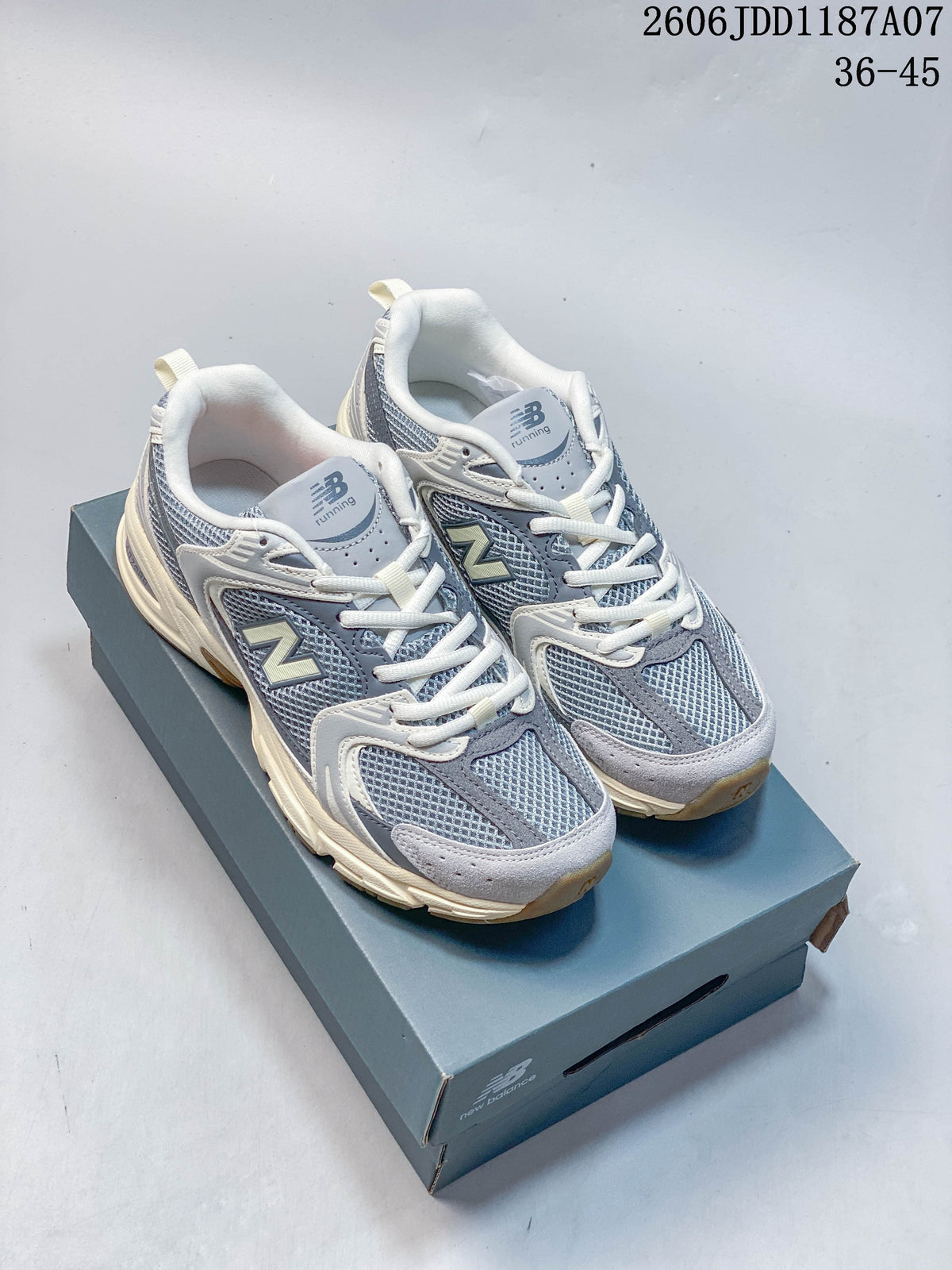 Pair of grey and blue-grey New Balance 530-style mesh sneakers with off-white accents, shown on a shoe box.