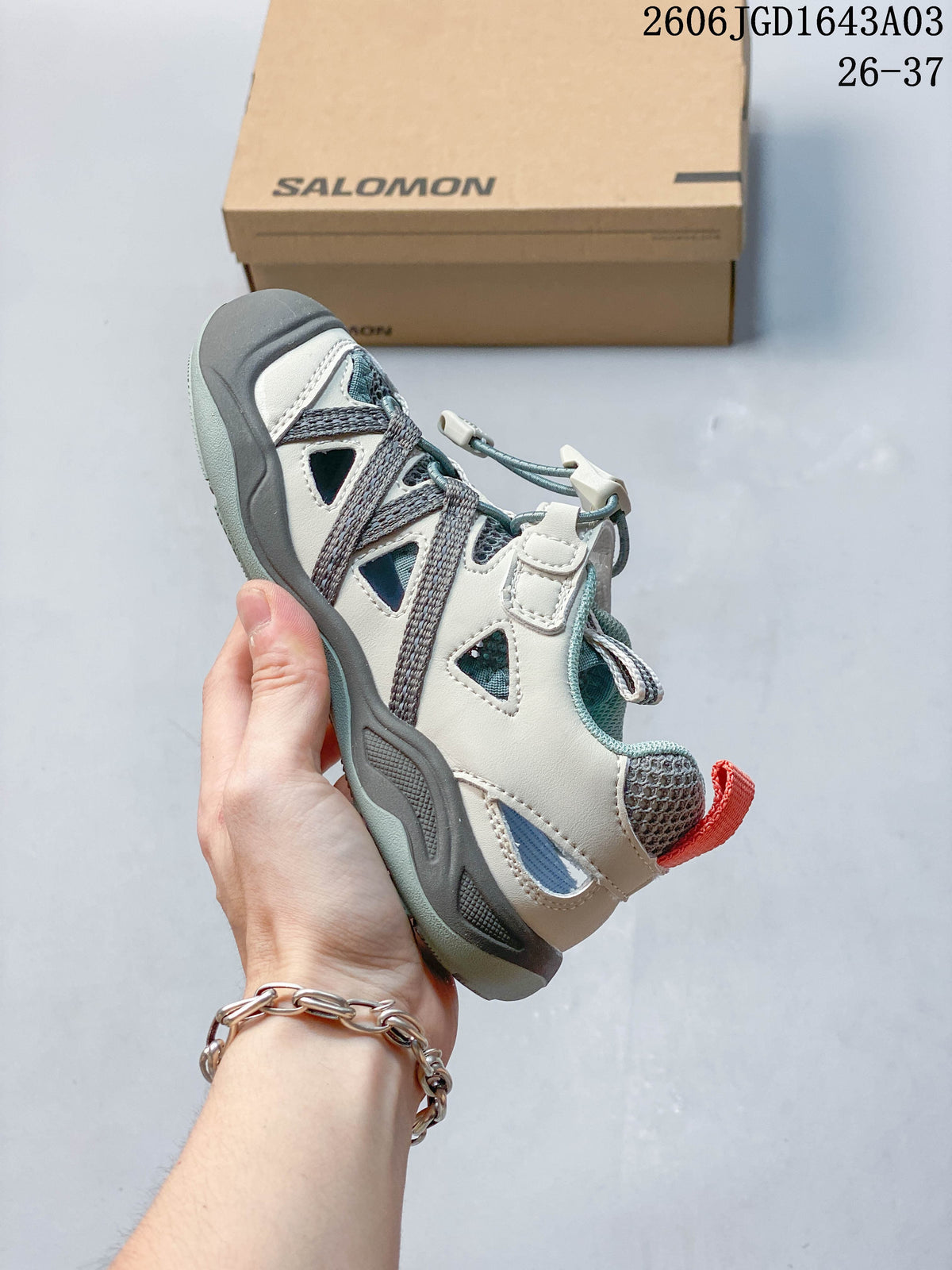 Side view of a cream and teal Salomon kids’ sneaker with a quick-lace closure.