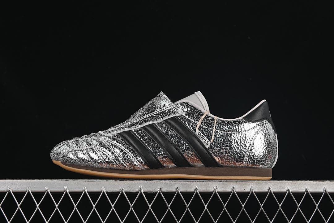 Side view of the silver metallic adidas Taekwondo W shoe with black stripes and forefoot strap.