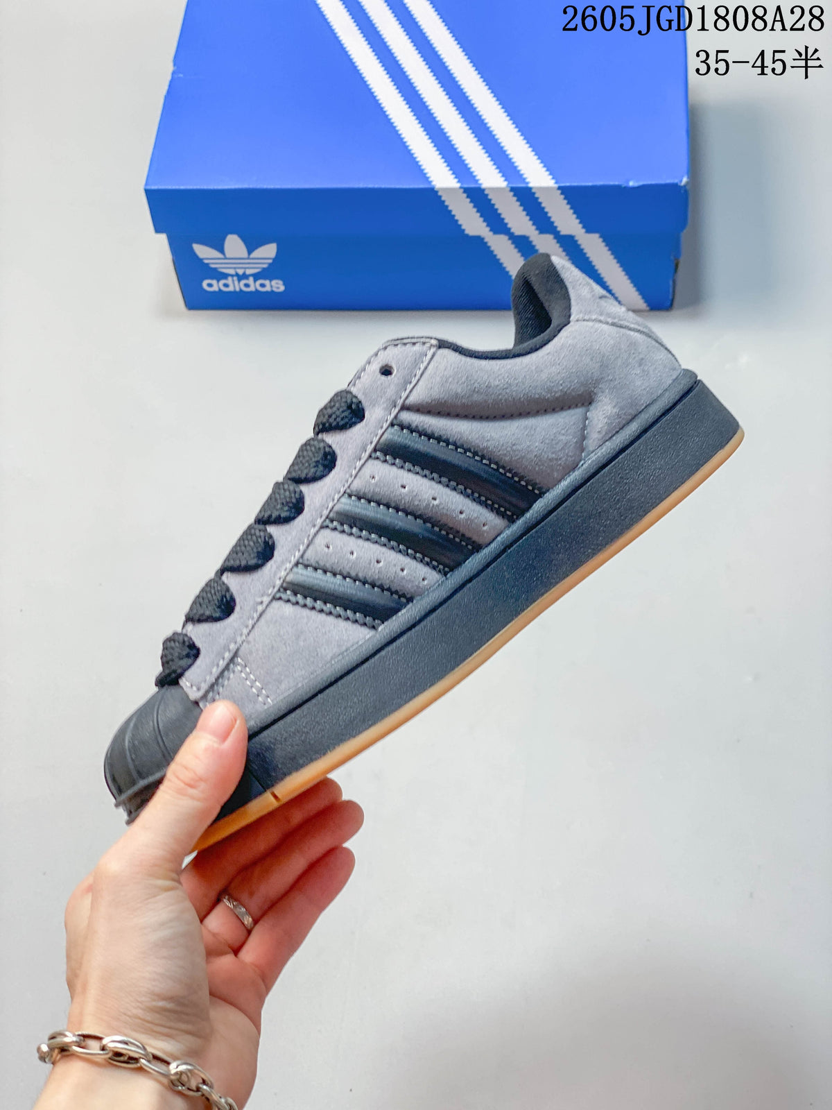 Side profile of the grey Superstar shoe with dark stripes, shell toe and gum outsole.