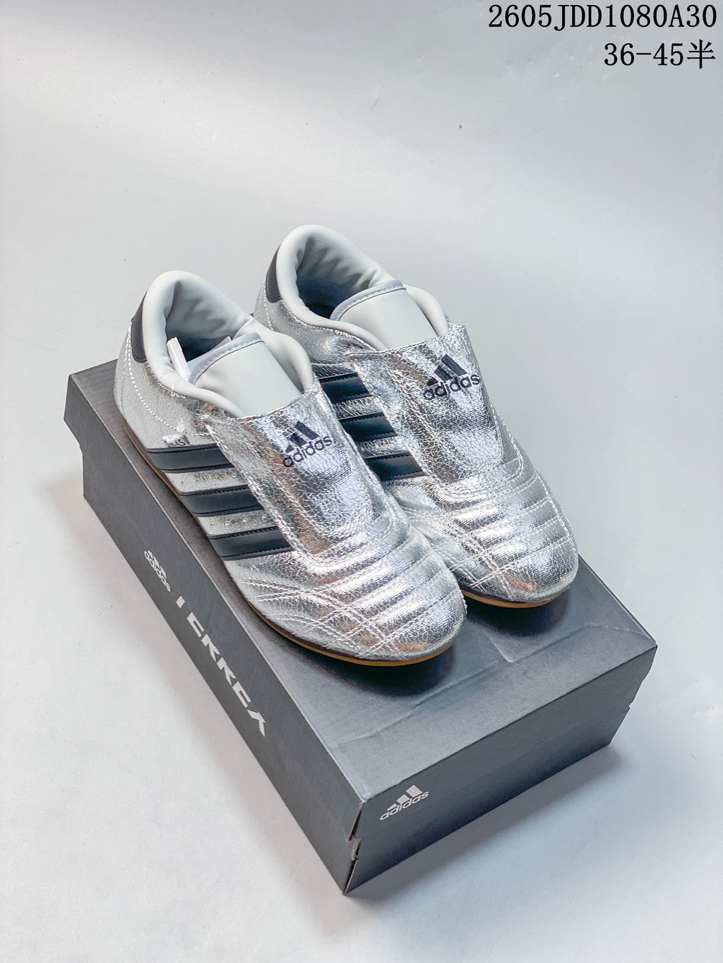 Pair of reflective silver Adidas Taekwondo shoes with dark stripes and gum-colored soles