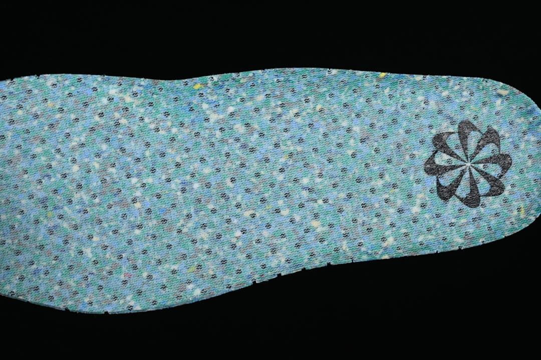 Reverse side of a blue-green patterned shoe insole with a small emblem.