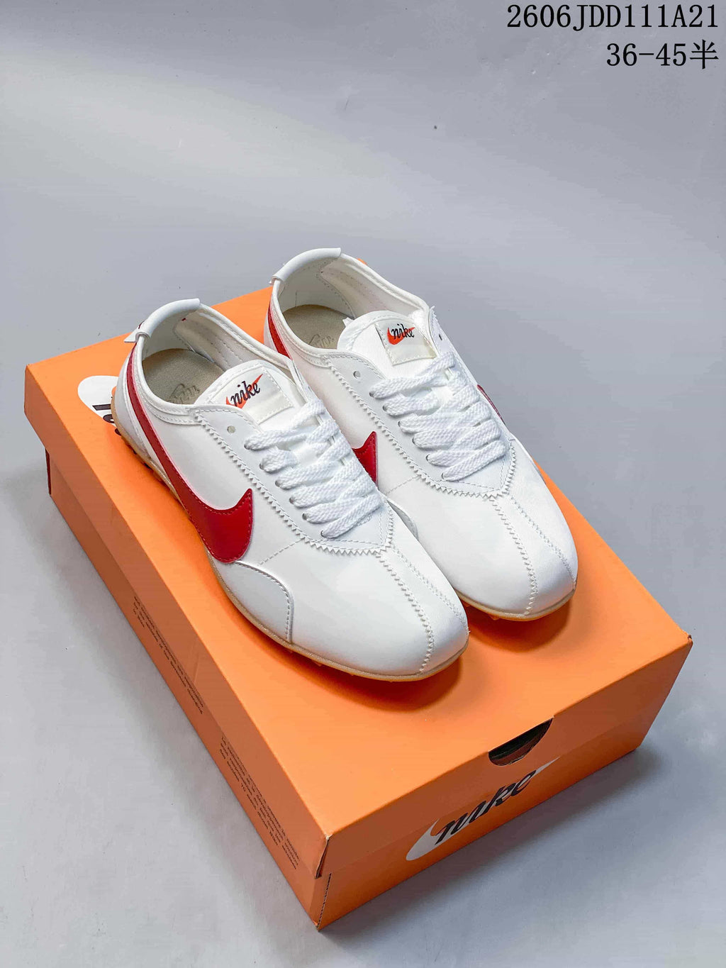 Pair of white Nike Moon Shoe OG Summit low-top sneakers with red side detailing on an orange box