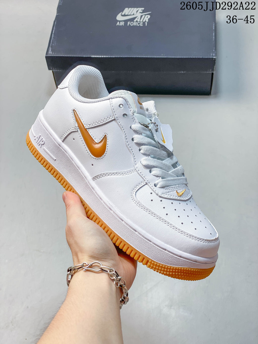 White low-top sneaker with gold-tone Swoosh details and an orange outsole