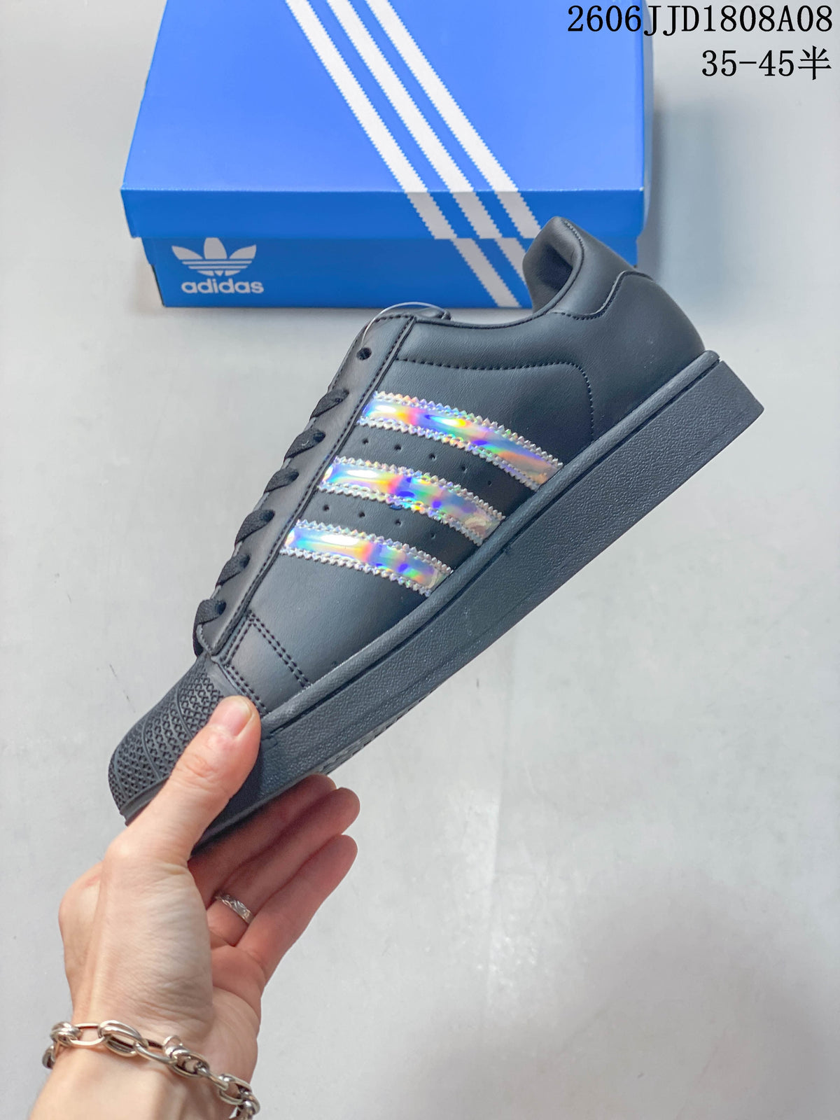 Side profile showing the charcoal Adidas Superstar and iridescent three stripes.
