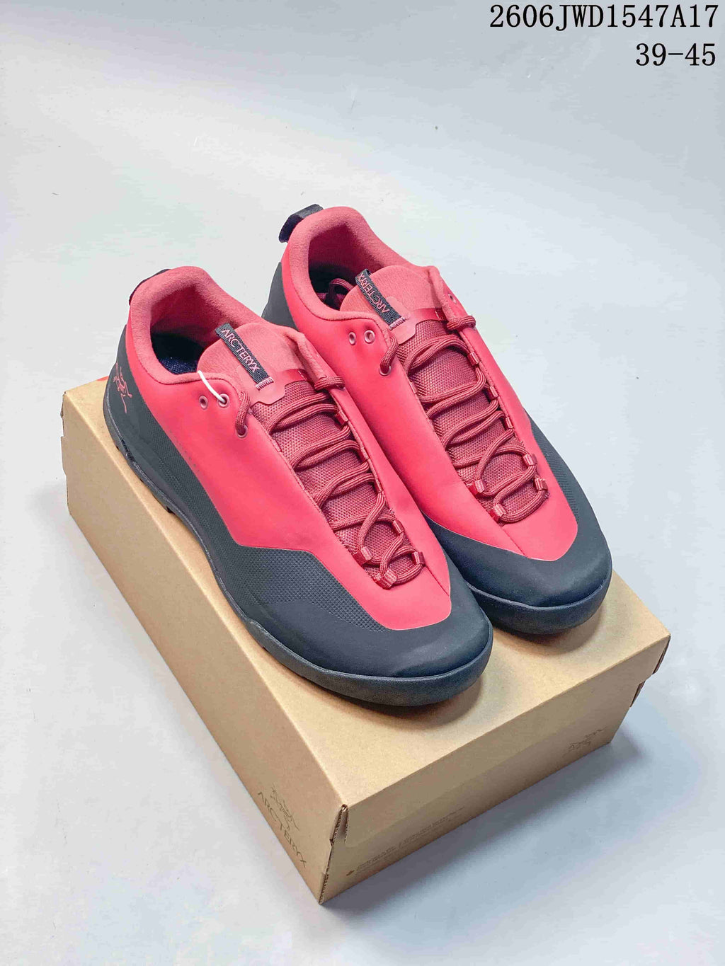 Pair of coral-red and charcoal Arc'teryx Konseal low-top shoes on a box
