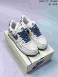 Pair of white and navy Nike Air Force 1 '07 Low sneakers with patterned laces and gold-tone lace accessory on a shoe box.