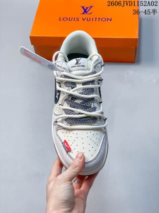 Top view of a white and gray Louis Vuitton x Nike Dunk Low sneaker with red accents, dark blue patterned panels, and an orange branded box behind it.