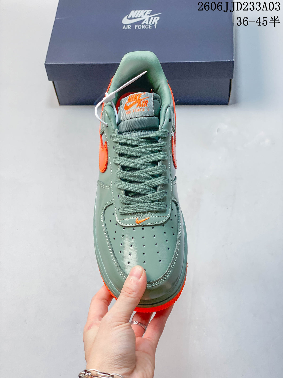 Front view of a green Air Force 1 ’07 sneaker with perforated toe and orange details