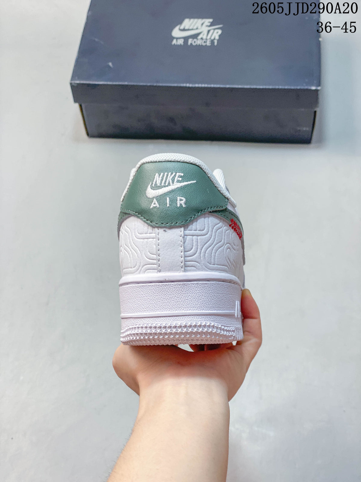 Rear view of a white sneaker with a green heel tab and embossed patterned panels.