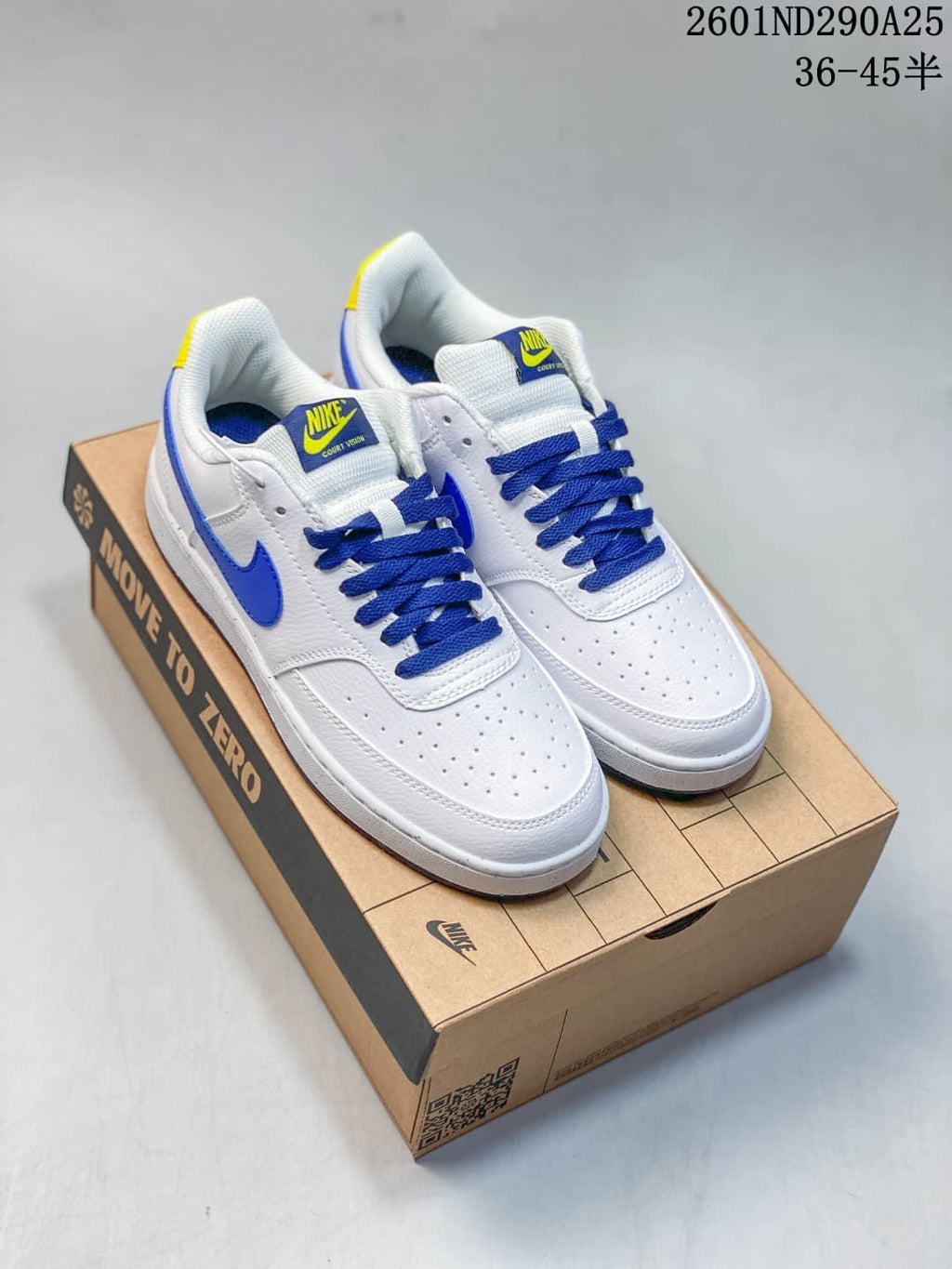 Pair of white Nike Court Vision Low sneakers with blue laces and accents and yellow details, shown on a shoebox.