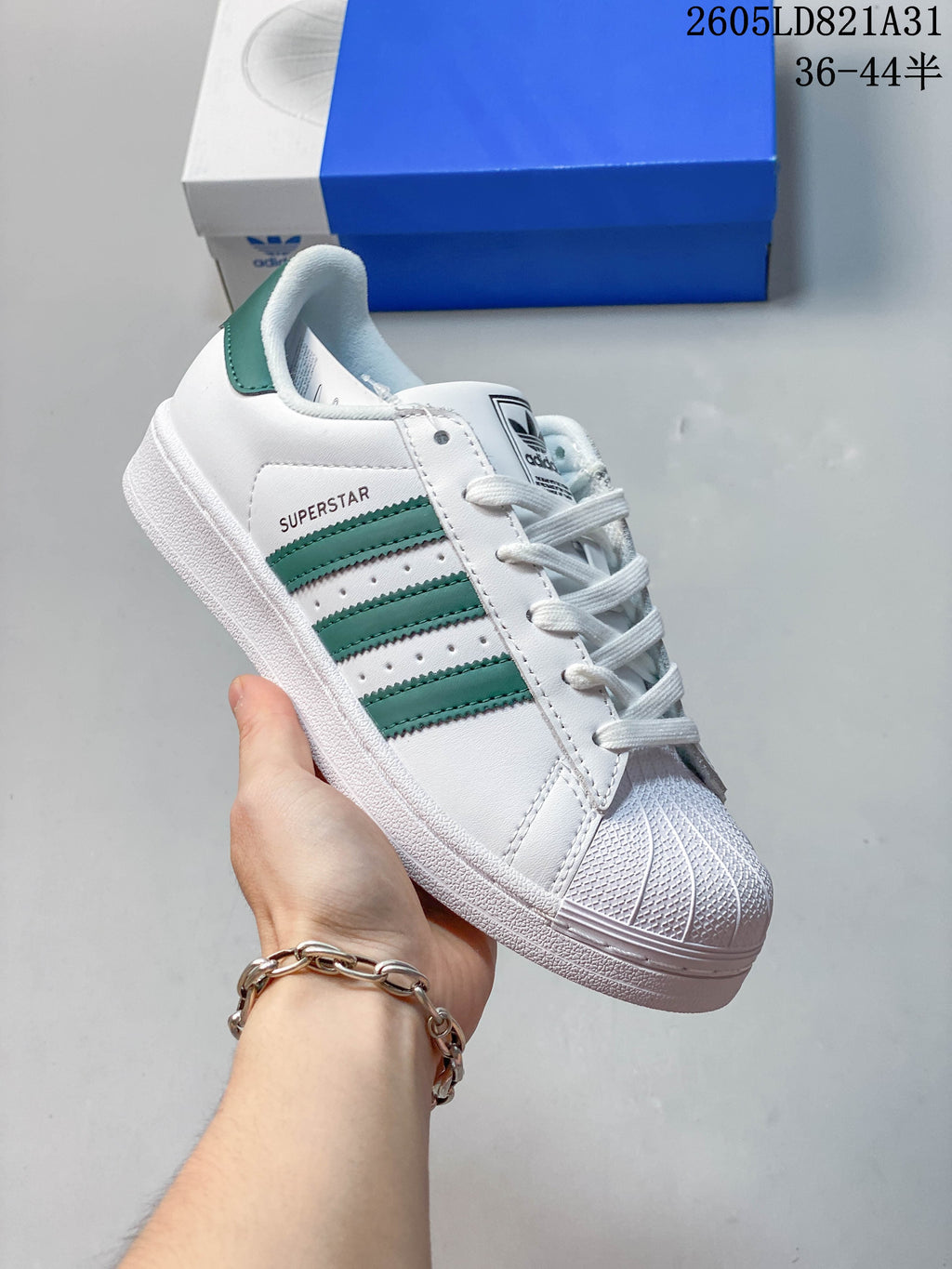 White adidas Superstar sneaker with green stripes and a textured shell toe.