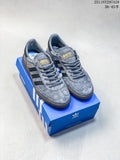 Pair of gray Adidas Handball Spezial sneakers with black stripes and brown outsoles, shown on a blue box