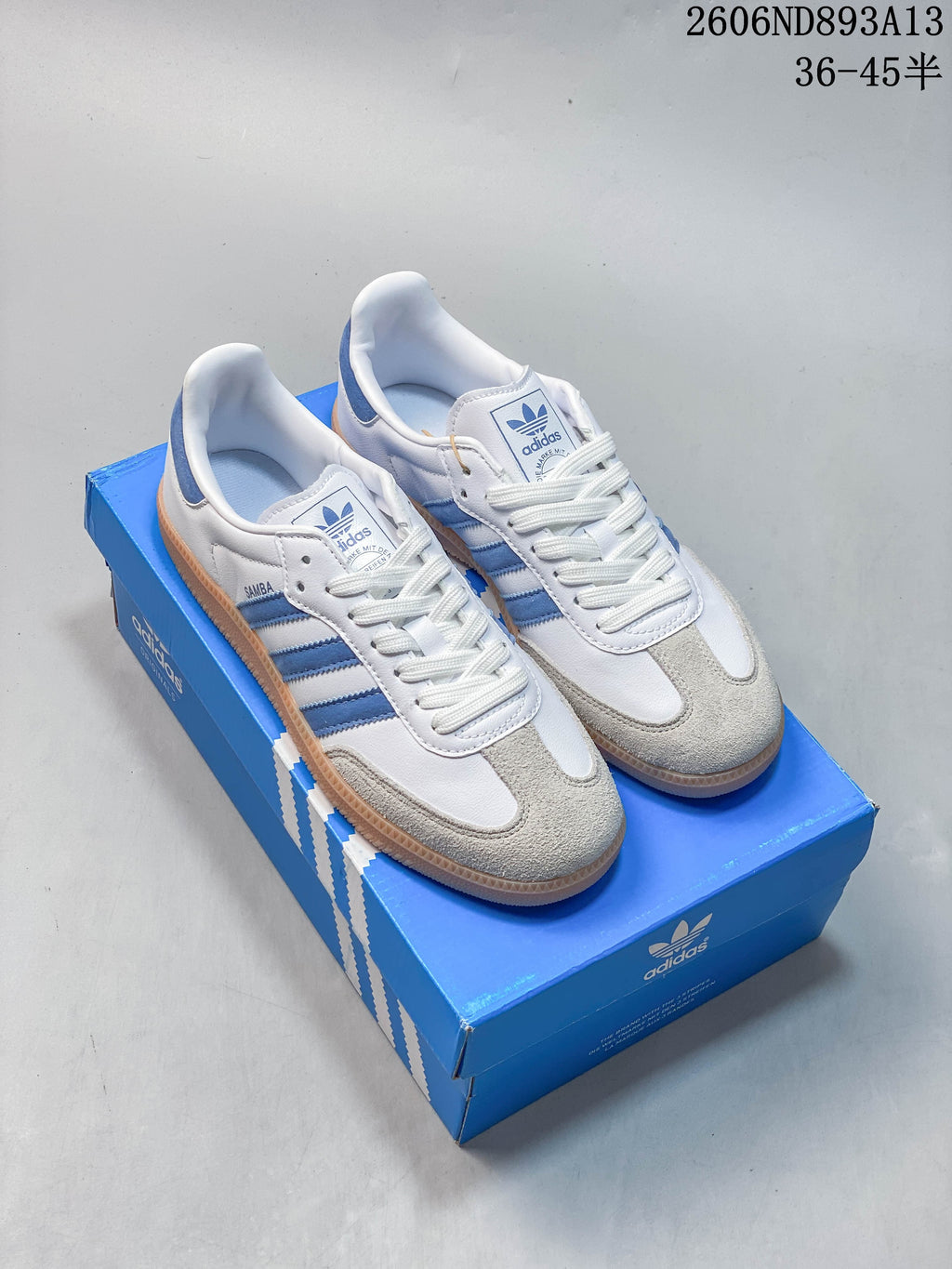 White and blue adidas Samba OG low-top sneakers with a gum-colored outsole, shown on a blue shoe box.