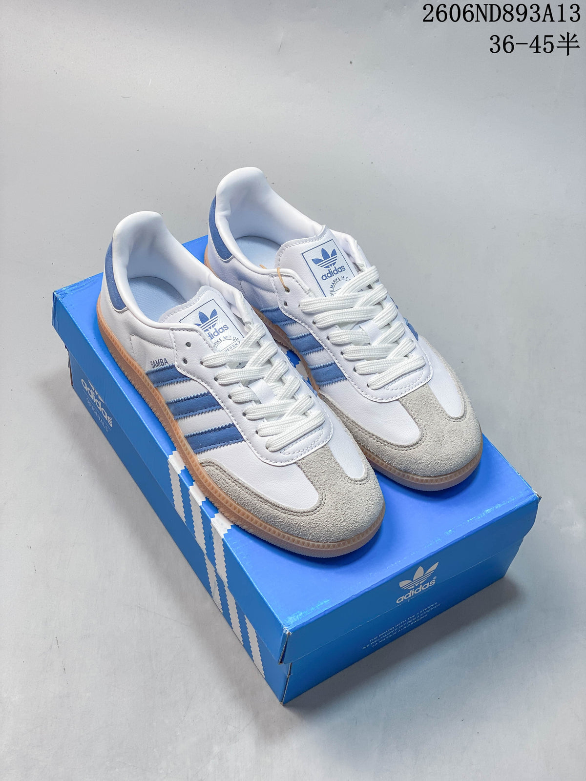 White and blue adidas Samba OG low-top sneakers with a gum-colored outsole, shown on a blue shoe box.