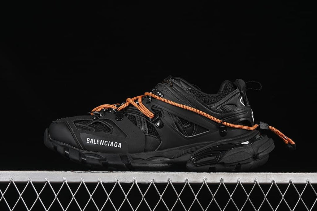 Black sneaker with orange laces shown in side profile.