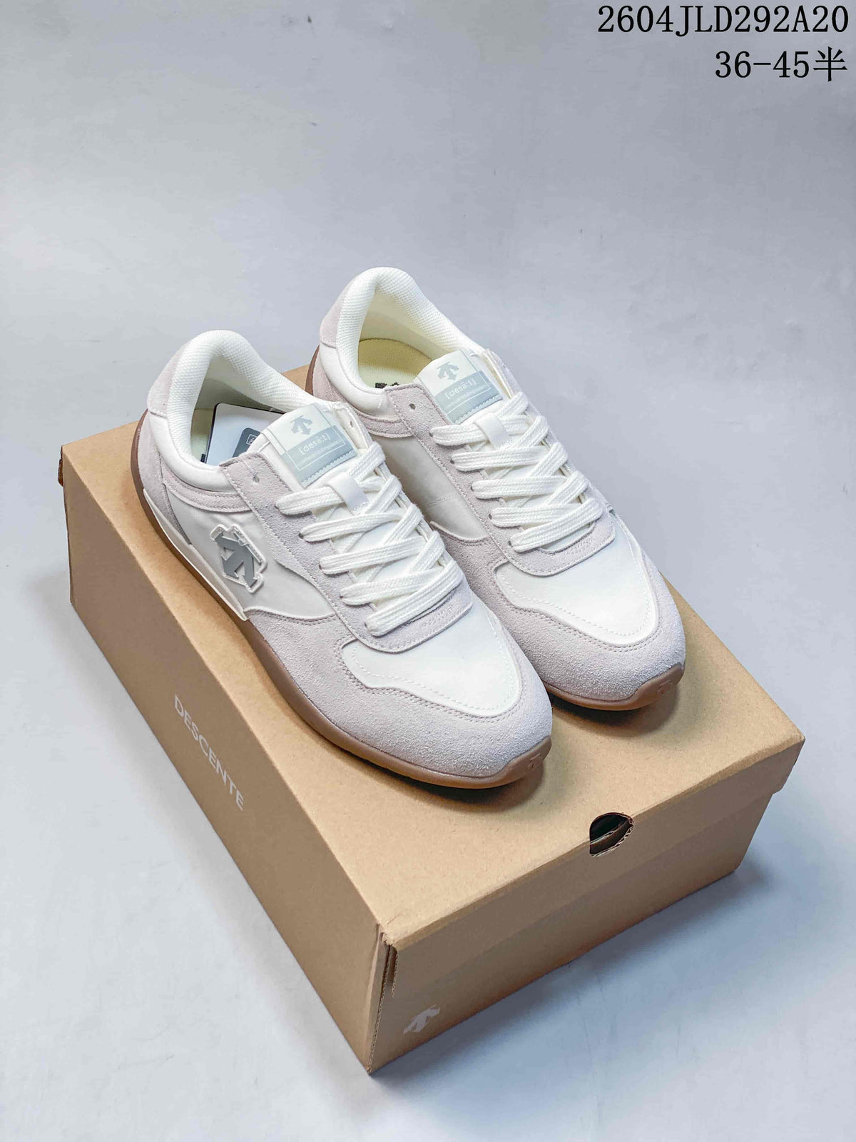 White and pale gray Descente low-profile sneakers with gum-tone soles, shown on a branded shoebox.