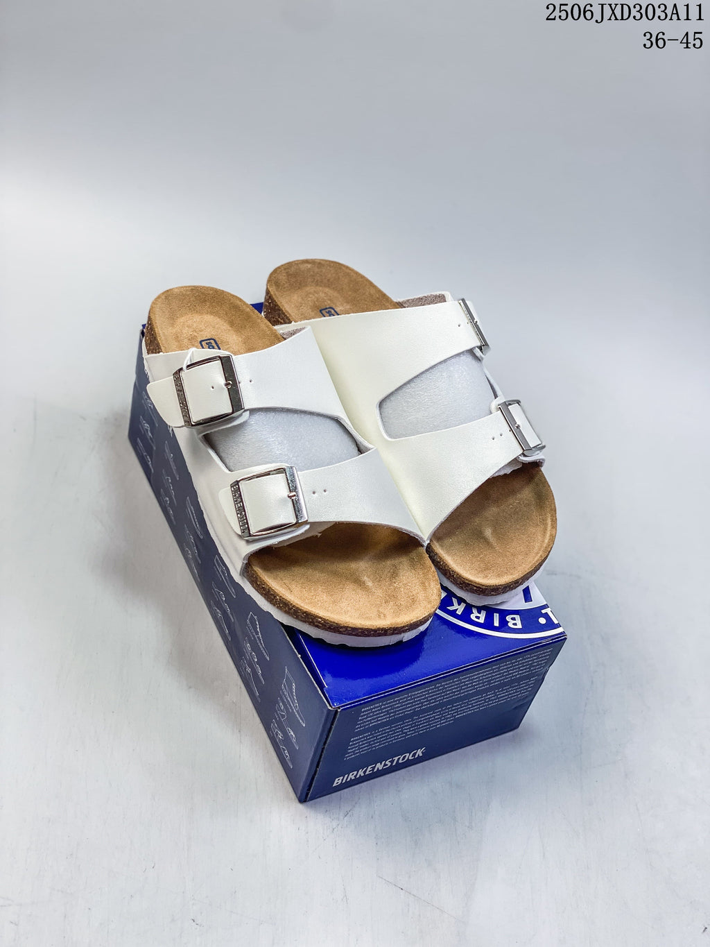 White two-strap slide sandals with silver-tone buckles and brown contoured footbeds, shown on a blue box.