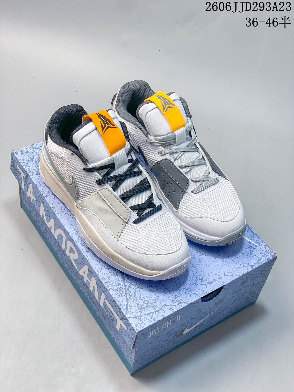 Pair of white and gray Nike Ja 1 EP shoes with dark laces and yellow-orange tongue details, displayed on a blue box.