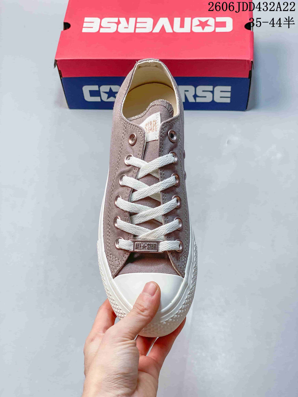 Top view of a taupe Converse sneaker with white laces, metal eyelets, and a rubber toe cap