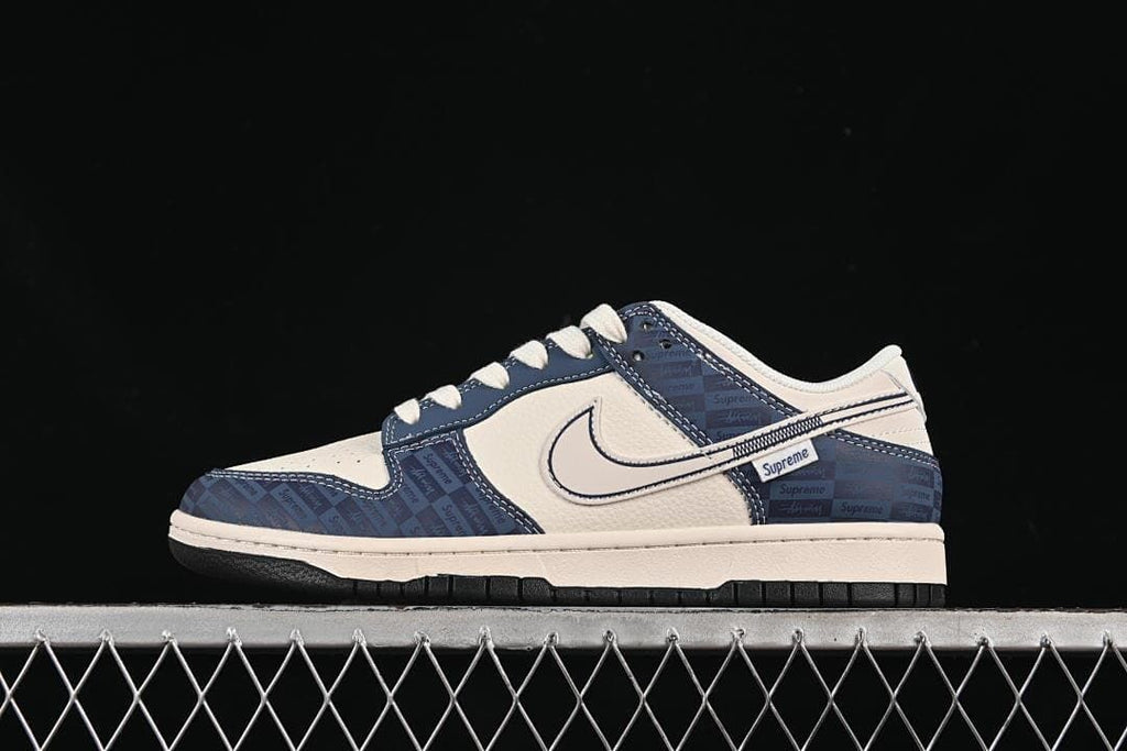 Side view of a cream and navy Nike SB Dunk Low with a repeating wordmark pattern on the overlays.