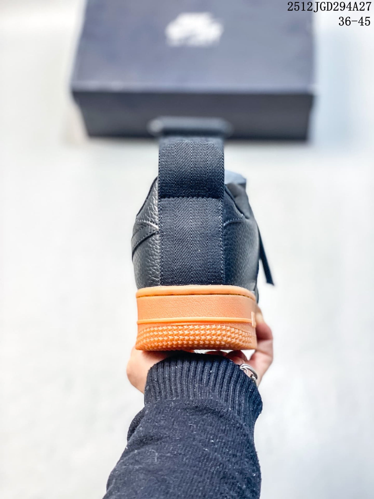 Rear view of a black low-top sneaker with an orange heel section and pull tab