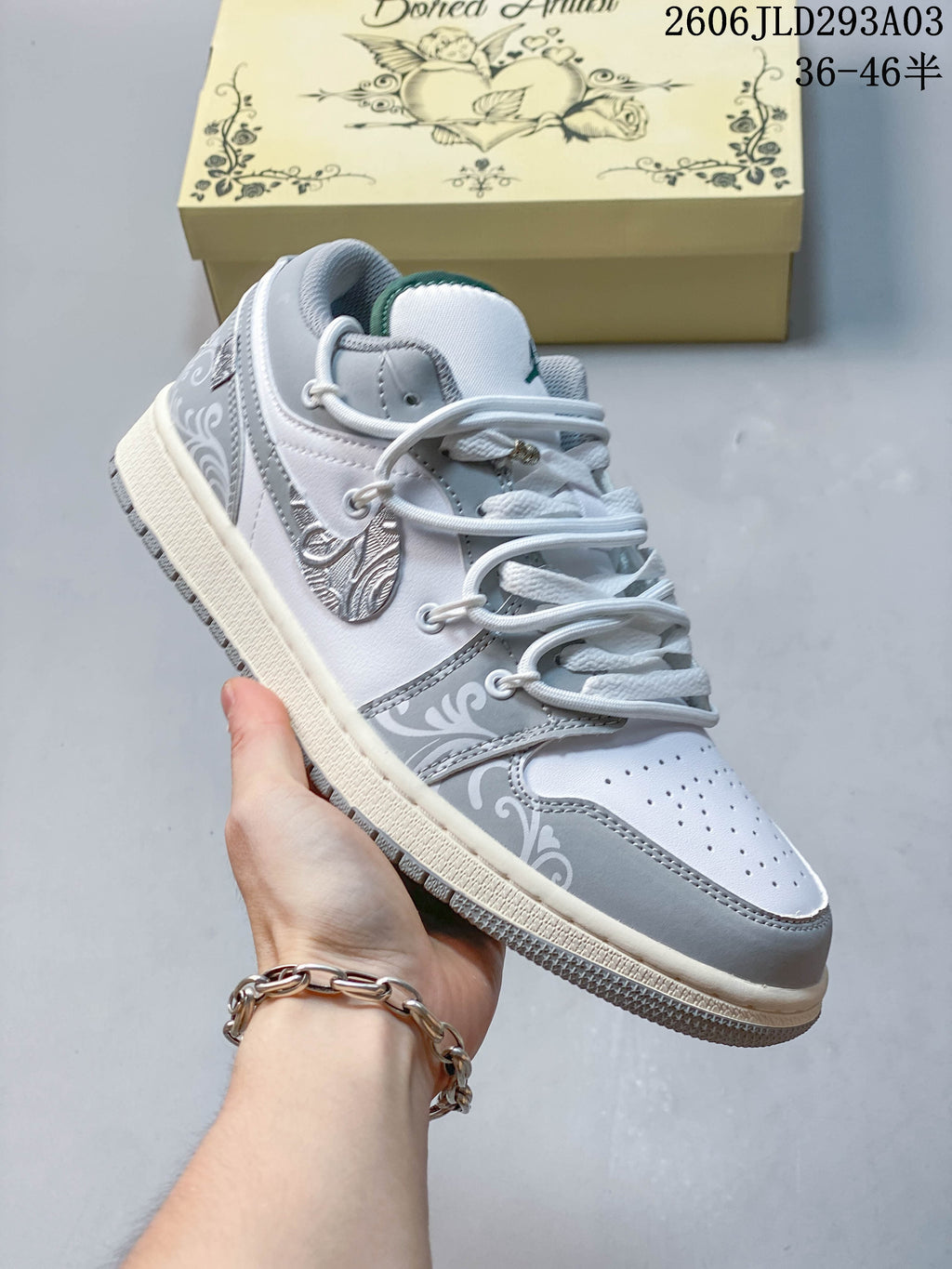 Angled side view of a white and gray Jordan low-top sneaker with decorative panels and a green tongue accent; overlay shows a size range.