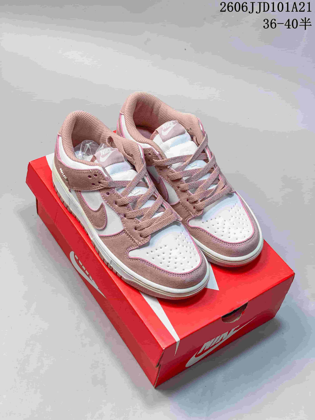 Pair of pink and white Nike Dunk Low SB-style sneakers viewed from above on a red shoe box.
