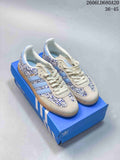 Pair of blue-and-cream floral Adidas Samba OG sneakers with gum-colored soles, shown on a blue box.