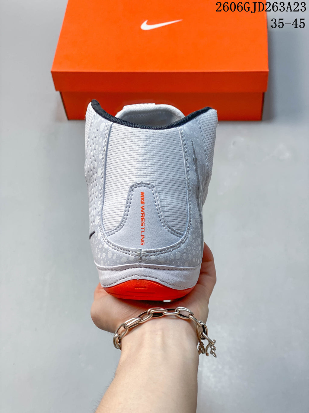 Rear view of a white and light gray Nike Inflict 4 shoe with bright orange heel detail.