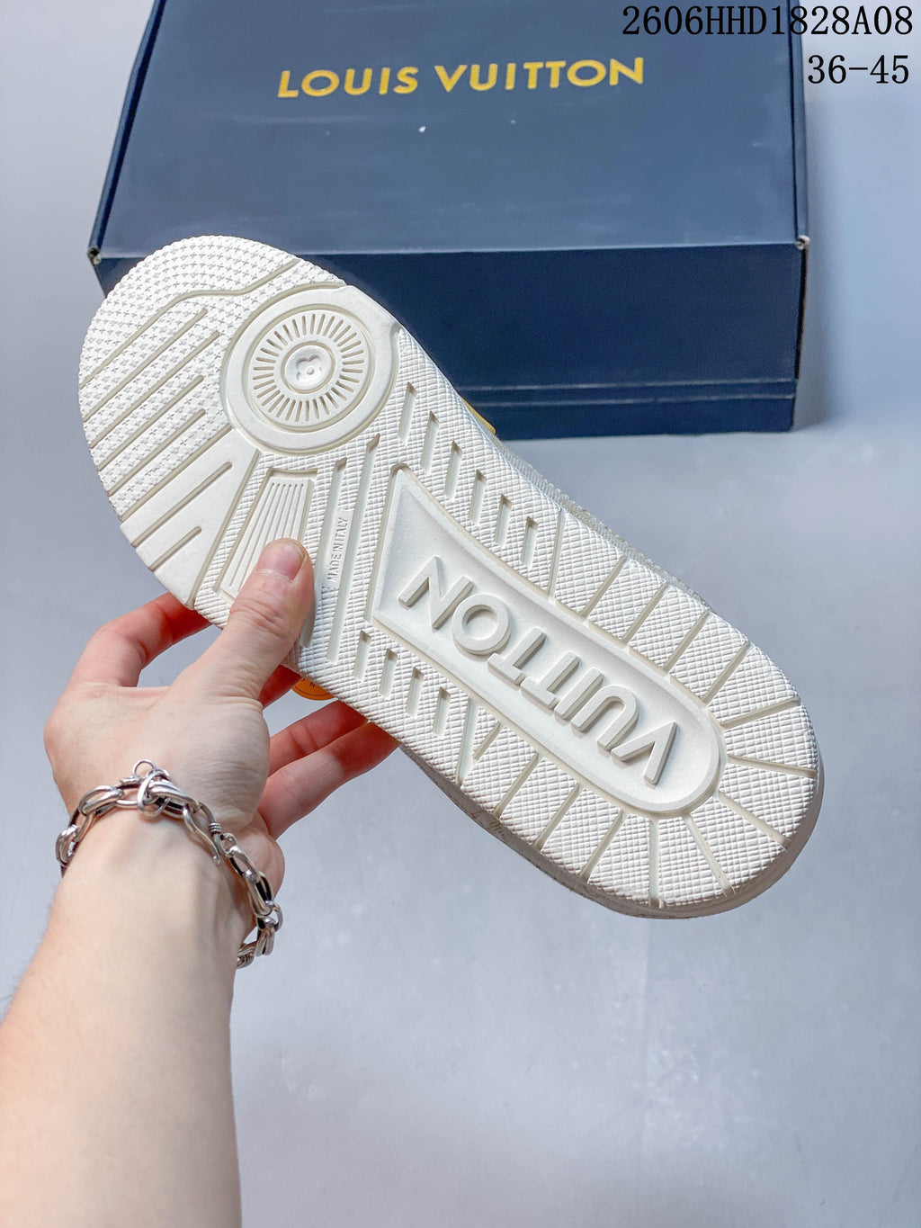 Treaded outsole of a white sneaker, with a dark blue branded box in the background.