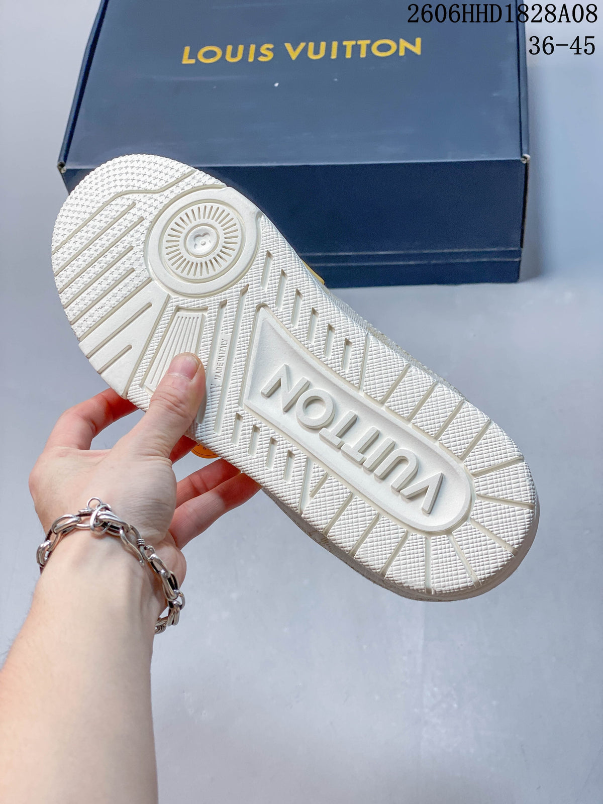 Treaded outsole of a white sneaker, with a dark blue branded box in the background.