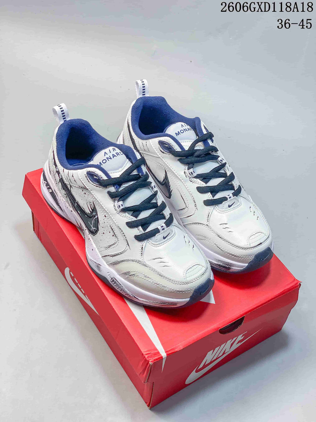 Pair of white and navy Nike Air Monarch sneakers with graphic detailing, shown on a red shoe box.