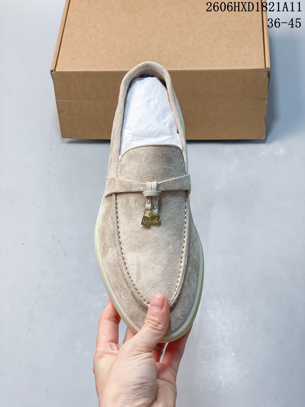 Top view of a beige loafer with moc-toe stitching and small metal lock accents.