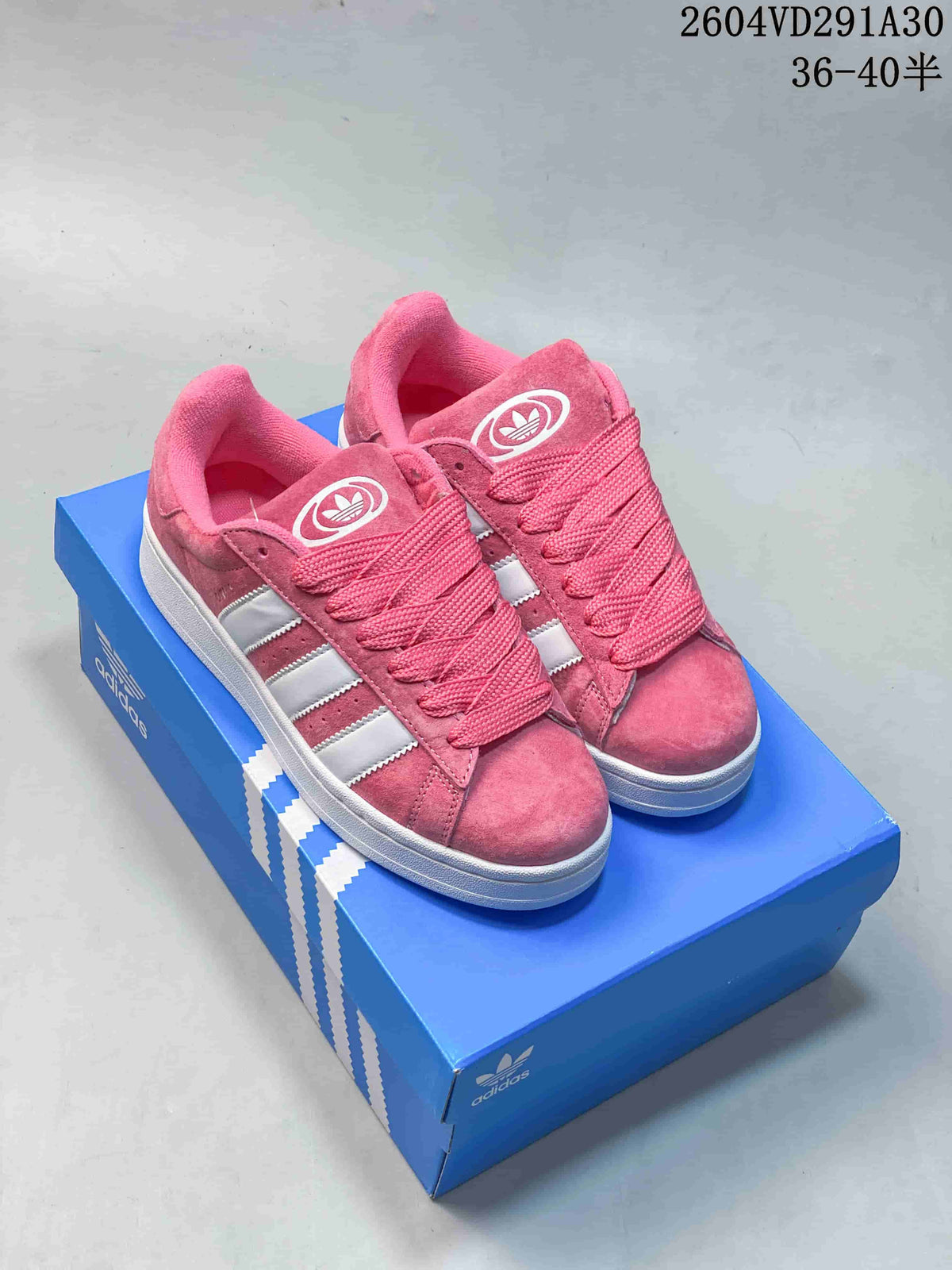 Pair of pink Adidas Campus 00s low-top sneakers with white stripes and white soles, shown on a blue box.