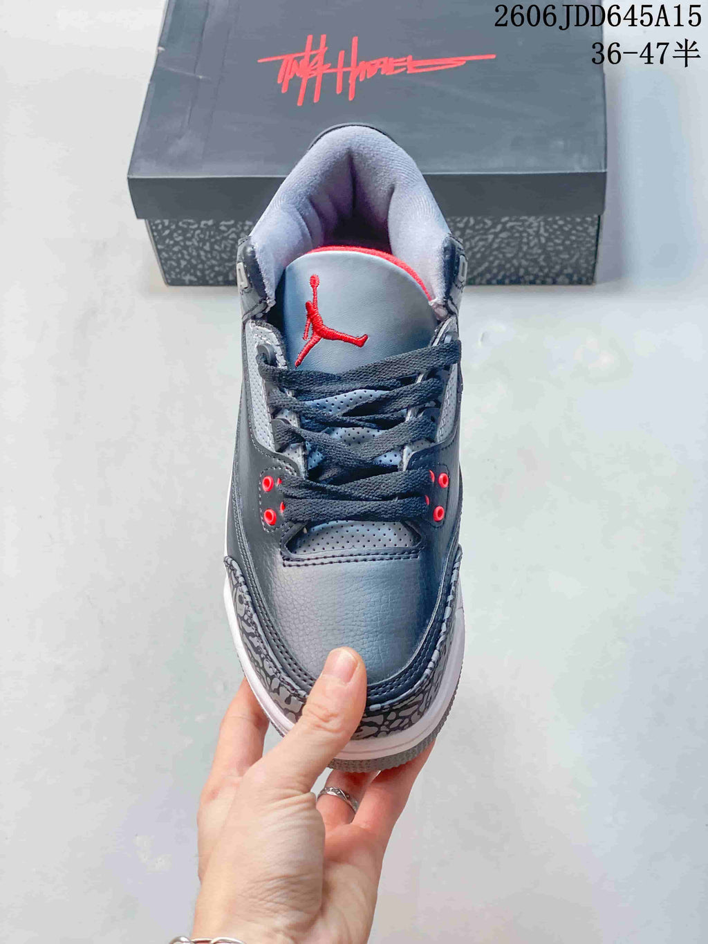Front view of a grey sneaker showing dark laces, red eyelets, and a red tongue logo.