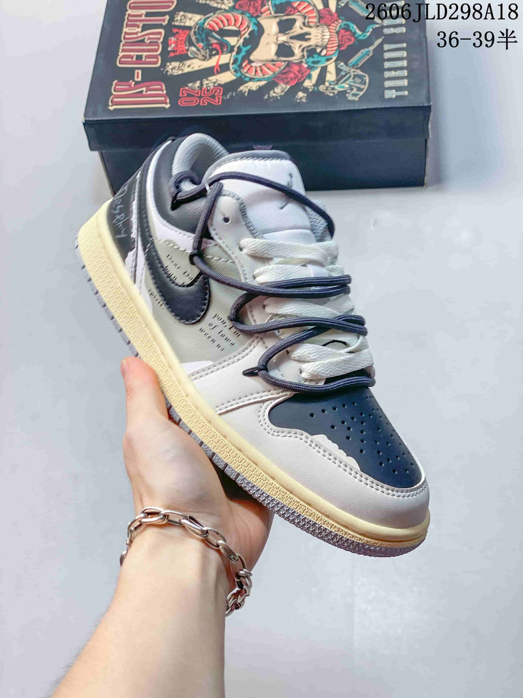 Angled side view of a gray and white Air Jordan 1 Low sneaker with a dark Swoosh and light-colored midsole.