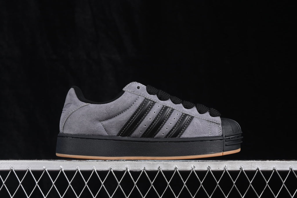 Side profile showing the grey upper, black three-stripe detailing, shell toe, black midsole, and gum outsole.