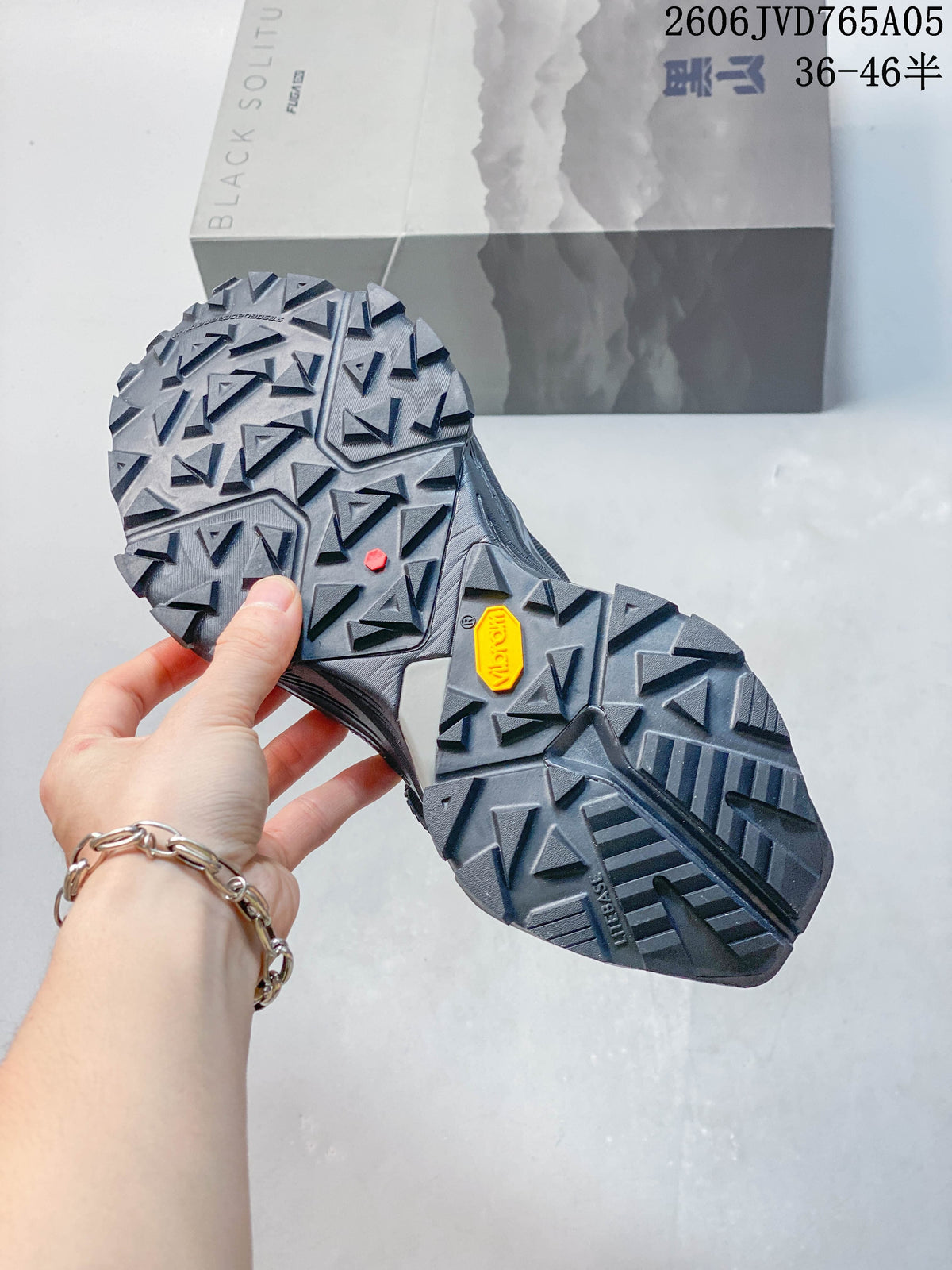 Close view of the trail shoe outsoles with deep angular tread and a visible Vibram logo.