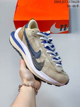 Angled side view showing the beige mesh-like upper, layered Swoosh detailing, blue accents, and stacked midsole.